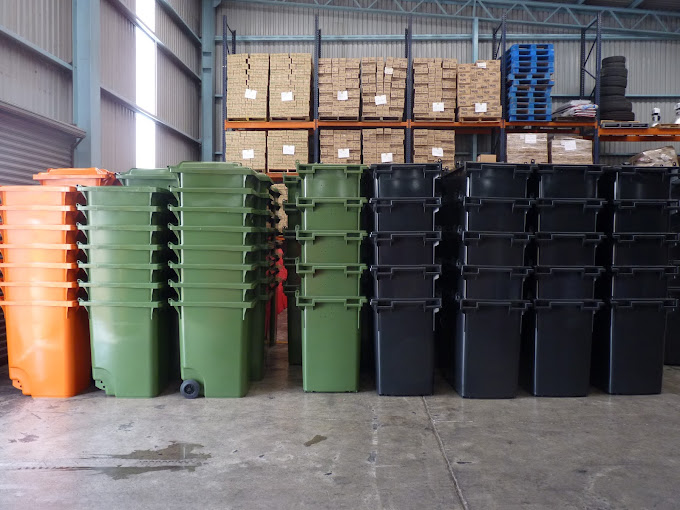 Contenedores de basura de colores naranja, verde y negro. Los productos se encuentran apilados en una bodega.